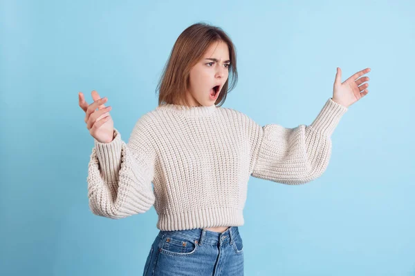 Immagine dinamica di giovane ragazza beuatiful, studente in abiti casual apre la bocca a sorpresa isolato sul backgroud studio azzurro. — Foto Stock