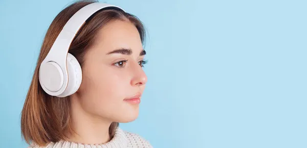 Side view of young cute girl, student in casual clothes listening to music isolated on light blue studio backgroud. — Stock Photo, Image