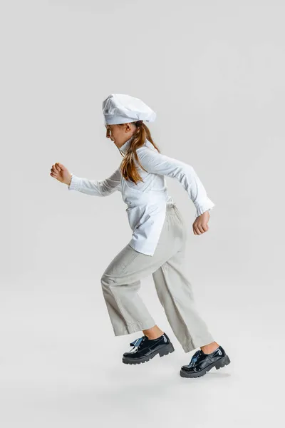 Маленька кавказька дівчинка в білій куховарській формі і величезні капелюхи шеф-кухарів ізольовані на білій студії. — стокове фото