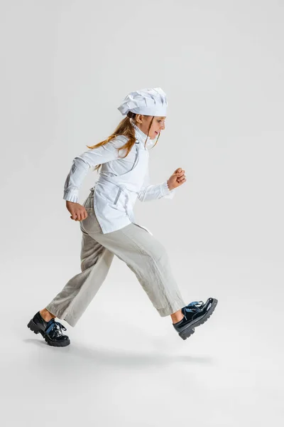 Pequena menina caucasiana em branco cozinhar uniforme e enorme chapéu de chefs indo isolado no fundo do estúdio branco. — Fotografia de Stock