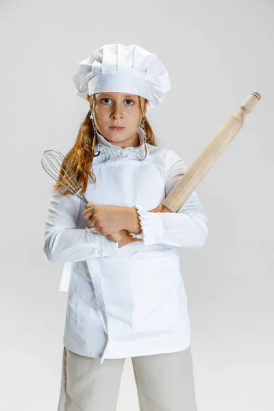 One little cute girl in white cook uniform and huge chefs hat posing isolated on white studio background. — ストック写真
