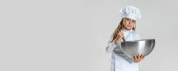 Volantino con la piccola ragazza carina in uniforme cuoco bianco ed enorme cuochi cappello posa isolato su sfondo bianco studio. — Foto Stock