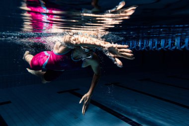 Sualtı çatışması. Bir bayan yüzücü havuzda, kapalı alanda eğitim görüyor. Yüzme hareketlerinin sualtı görüntüsü ayrıntıları.