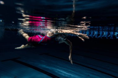 Yüzme şapkalı ve gözlüklü bir bayan yüzücü bilardo salonunda, kapalı alanda antrenman yapıyor. Yüzme hareketlerinin sualtı görüntüsü ayrıntıları.