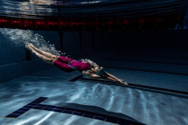 Sualtı çatışması. Bir bayan yüzücü havuzda, kapalı alanda eğitim görüyor. Yüzme hareketlerinin sualtı görüntüsü ayrıntıları.