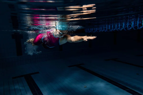 一名戴着泳帽和护目镜的女游泳者在室内游泳池接受训练。游泳运动的水下景观详情. — 图库照片