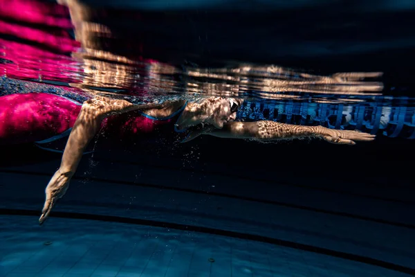 Nadadora femenina de primer plano con gorra de natación y gafas de entrenamiento en la piscina, en interiores. Vista submarina de los movimientos de natación detalles. — Foto de Stock