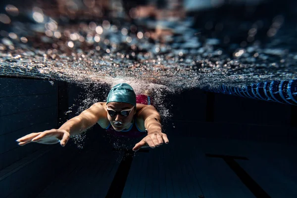 Unterwasser-Ansicht der Schwimmbewegungen Details. Eine Schwimmerin mit Badekappe und Schwimmbrille beim Schwimmtraining im Hallenbad. — Stockfoto