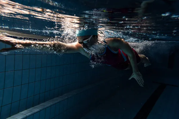 Jedna pływaczka w czapce kąpielowej i gogle trening na basenie, w pomieszczeniu. Podwodny widok ruchów pływackich szczegóły. — Zdjęcie stockowe