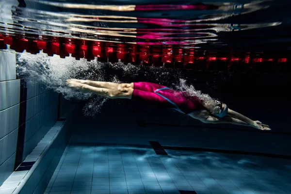 水下射击。一名女子游泳运动员在室内游泳池接受训练。游泳运动的水下景观详情. — 图库照片