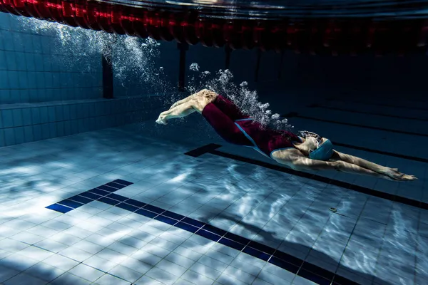Una nadadora con gorra de natación y gafas entrenando en la piscina, en interiores. Vista submarina de los movimientos de natación detalles. — Foto de Stock