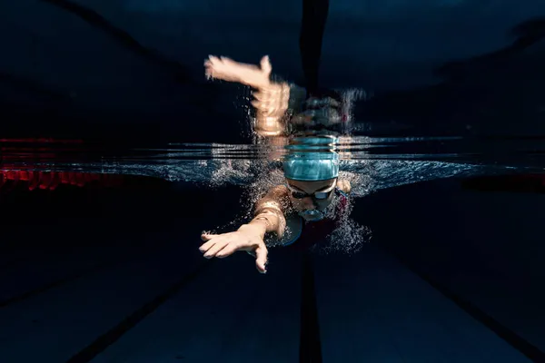 Nadadora profesional en gorra de natación y gafas en movimiento y acción durante el entrenamiento en la piscina, en interiores. Disparos submarinos — Foto de Stock