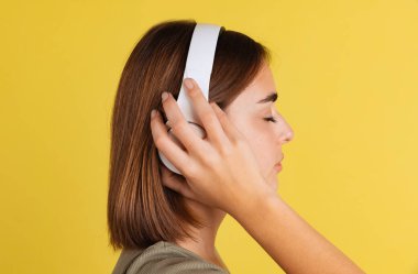 Beyaz kulaklıklı bir öğrenci sarı stüdyo arka planında izole edilmiş müzik dinliyor..