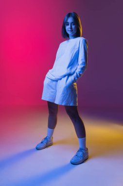 Genç ve güzel bir kızın stüdyo çekimi, gündelik giyinen bir öğrenci pembe-mor gradyan stüdyo arka planında izole edilmiş gözlerle bakıyor..