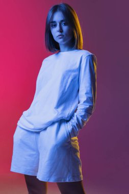 Genç ve güzel bir kızın stüdyo çekimi, gündelik giyinen bir öğrenci pembe-mor gradyan stüdyo arka planında izole edilmiş gözlerle bakıyor..