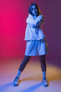 Genç ve güzel bir kızın stüdyo çekimi, gündelik giyinen bir öğrenci pembe-mor gradyan stüdyo arka planında izole edilmiş gözlerle bakıyor..