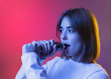 Genç kız, genç kız ya da beyaz giysili öğrenci şarkı söylüyor. Pembe-mırıltılı arka planda, neon ışıkta izole edilmiş.