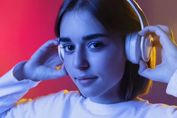 若いかわいい女の子のクローズアップポートレート,学生のカジュアルな服に耳を傾け音楽に隔離されたピンク紫色のスタジオバックネオンで. — ストック写真