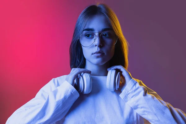 Studio shot van jong serieus meisje, student in casual slijtage staten bij blik geïsoleerd op roze-paars gradiënt studio backgroud in neon. — Stockfoto