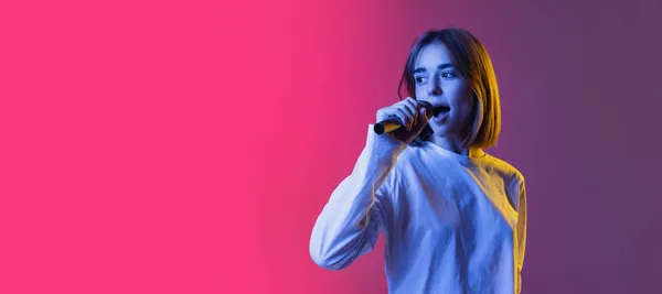 Flyer met mooi meisje, tiener of student in wit casual slijtage zingen geïsoleerd op roze-purplr gradiënt backgroud in neon licht — Stockfoto