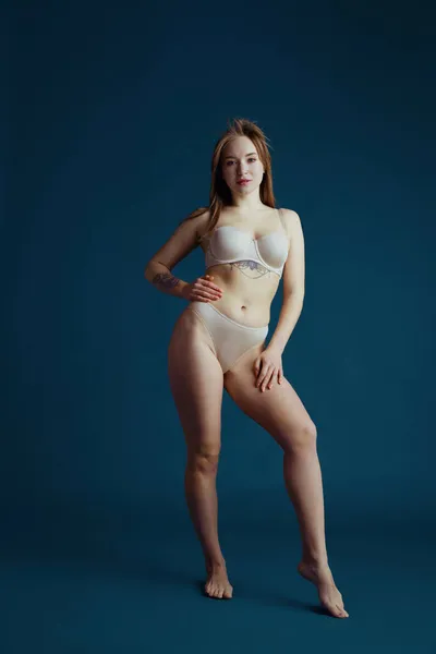 Portrait de jeune belle femme rousse en tenue intérieure posant isolée sur fond de studio bleu. Concept de beauté naturelle. — Photo