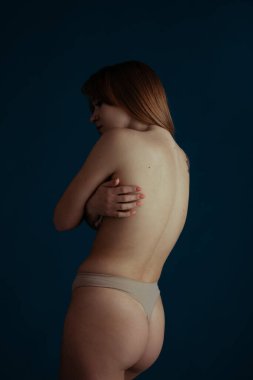 Klasik bir portre. Mavi arka planda, çıplak renkli iç çamaşırlı, güzel, kızıl saçlı bir kadın resmi..