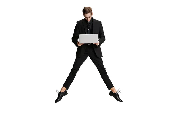 En stilig man i svart kostym flyger och använder laptop isolerad på vit bakgrund. Konst, inspiration koncept. — Stockfoto