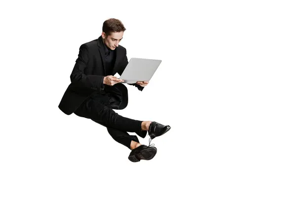 Um homem bonito em terno de negócios preto voando e usando laptop isolado no fundo branco. Arte, conceito de inspiração. — Fotografia de Stock