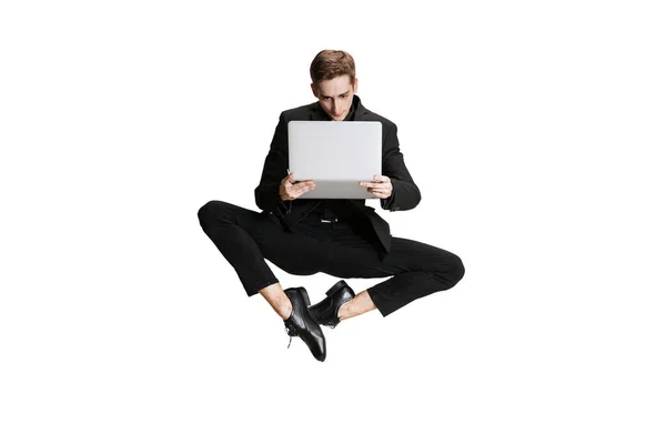 검은 정장을 입은 잘생긴 한 남자가 흰 배경에 컴퓨터를 단 채로 날라 다니며 컴퓨터를 사용하였습니다. 예술, 영감의 개념. — 스톡 사진