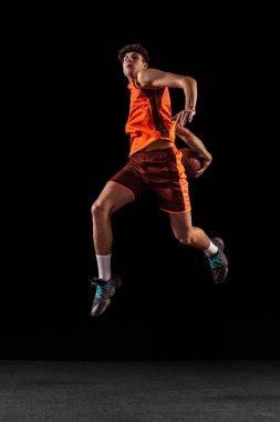 Basketbolcu eğitiminin tam boy portresi karanlık stüdyo arka planında izole edilmiş. Uzun boylu kaslı sporcu topla zıplıyor..