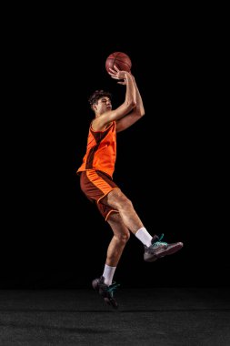 Basketbolcu eğitiminin tam boy portresi karanlık stüdyo arka planında izole edilmiş. Uzun boylu kaslı sporcu topla zıplıyor..