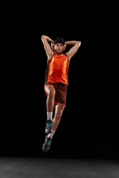 Ritratto completo di allenamento del giocatore di basket isolato su sfondo scuro studio. Alto atleta muscolare che salta con la palla. — Foto Stock