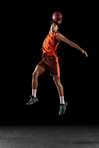 Volledig portret van basketbalspeler training geïsoleerd op donkere studio achtergrond. Groot gespierd atleet springen met bal. — Stockfoto