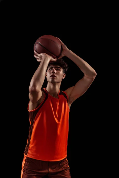 Studio shot di giovane uomo, giocatore di basket che fa set shot isolati su sfondo scuro studio. Sport, energia, potenza, risultati. — Foto Stock