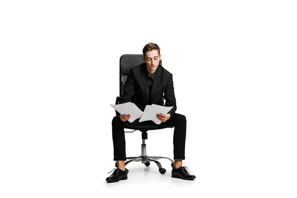 Portrait of young man in black business suit, office manager sitting on chair isolated on white background. Art, inspiration concept. — Stock Photo, Image