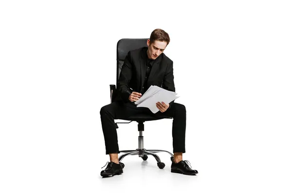 Portrait of young man in black business suit, office manager sitting on chair isolated on white background. Art, inspiration concept. — Stock Photo, Image