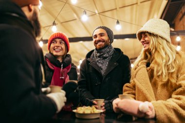 Mutlu gülümseyen arkadaşlar sıcak şaraplarla eğleniyorlar, kış festivalinde birlikte vakit geçiriyorlar. Tatiller, Noel konsepti
