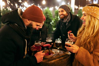 Genç mutlu insanlar, bira ve sosisli arkadaşlar eğleniyorlar, kış festivalinde birlikte vakit geçiriyorlar. Tatiller, Noel konsepti