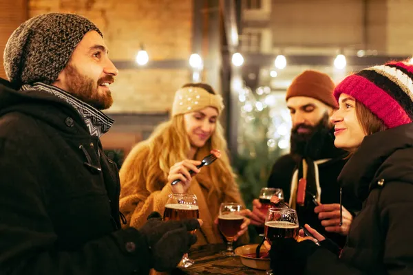 Happy smiling friends with cups of mulled wine having fun, spending time together at winter fair at evening. Holidays, Christmas concept Stock Picture