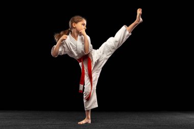 Küçük bir kızın portresi, genç bir karatenin karanlık arka planda tek başına çalışması. Spor, eğitim, beceri kavramı