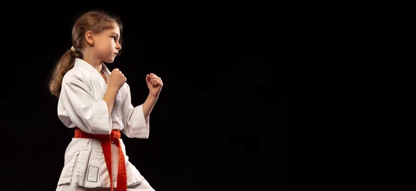 Een klein meisje, jong karate in vechtende houding geïsoleerd over donkere achtergrond. Begrip sport, onderwijs, vaardigheden — Stockfoto
