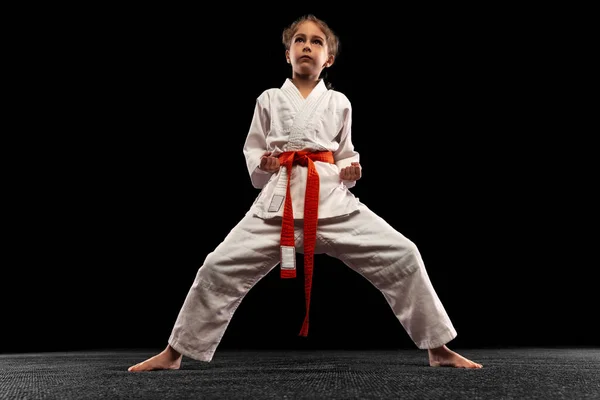 Egy kislány, fiatal karate harci pozícióban, elszigetelve a sötét háttérben. A sport, az oktatás és a készségek fogalma — Stock Fotó