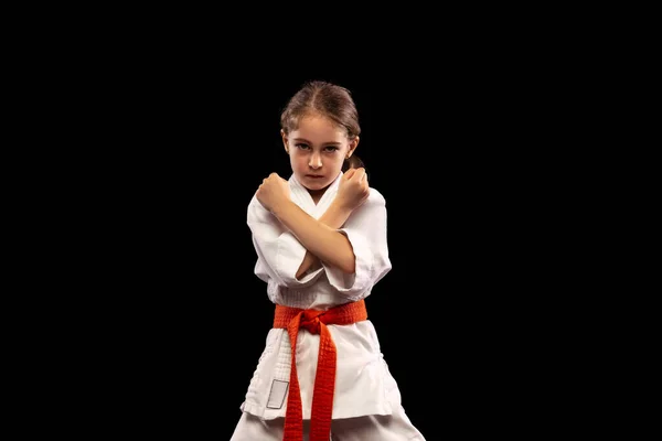 Portrait of little girl, young karate standing with crossed arms isolated over dark background. Concept of sport, education, skills — Stock Photo, Image