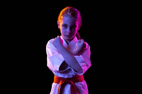 Portret van een klein meisje, jong karate met gekruiste armen geïsoleerd over donkere achtergrond. Begrip sport, onderwijs, vaardigheden — Stockfoto