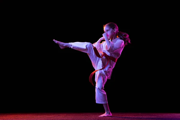 Portret van een klein meisje, jong karate dat alleen oefent, geïsoleerd over een donkere achtergrond. Begrip sport, onderwijs, vaardigheden — Stockfoto