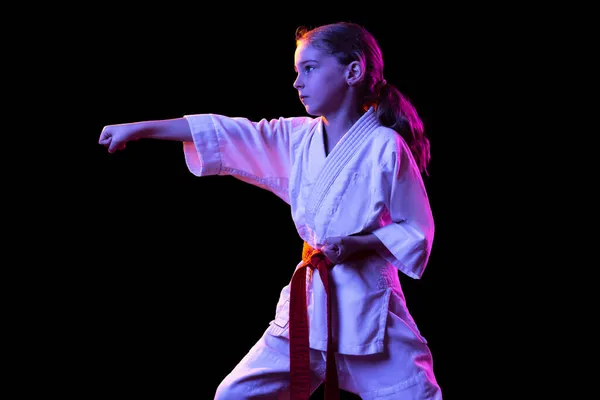 Een klein meisje, jong karate in kimono, die geïsoleerd oefent over een donkere achtergrond. Begrip sport, onderwijs, vaardigheden — Stockfoto