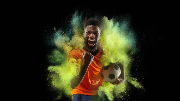 Kolaż z młodym sportowcem, piłkarzem w eksplozji kolorowego neonowego proszku odizolowanego na ciemnym tle — Zdjęcie stockowe