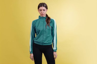 Yeşil eşofmanlı genç duygusal kızın portresi sarı stüdyo arka planında neon ışıkta izole edilmiş şekilde poz veriyor. Duygular, yüz ifadesi