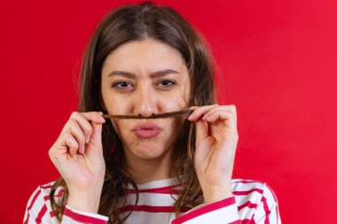 Kırmızı stüdyo arka planında yalnız poz veren hırkalı ve kot pantolonlu duygusal genç bir kız. Duyguların kavramı, yüz ifadesi