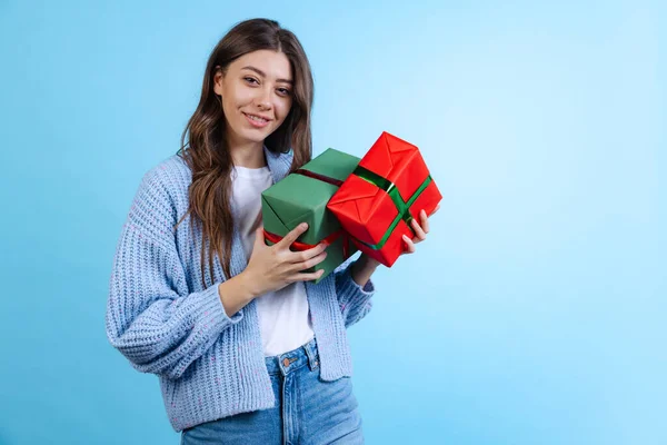 Podekscytowana młoda piękna dziewczyna trzyma pudełka z prezentami na niebieskim tle studia. Pojęcie emocji, Wesołych Świąt — Zdjęcie stockowe